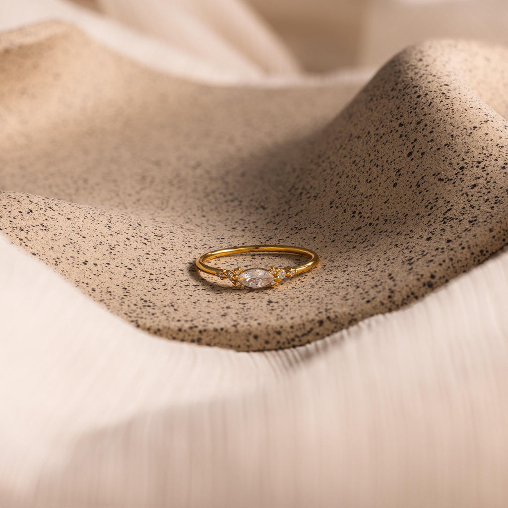 The Marquise Diamond Ring is displayed elegantly on a textured beige fabric surface.