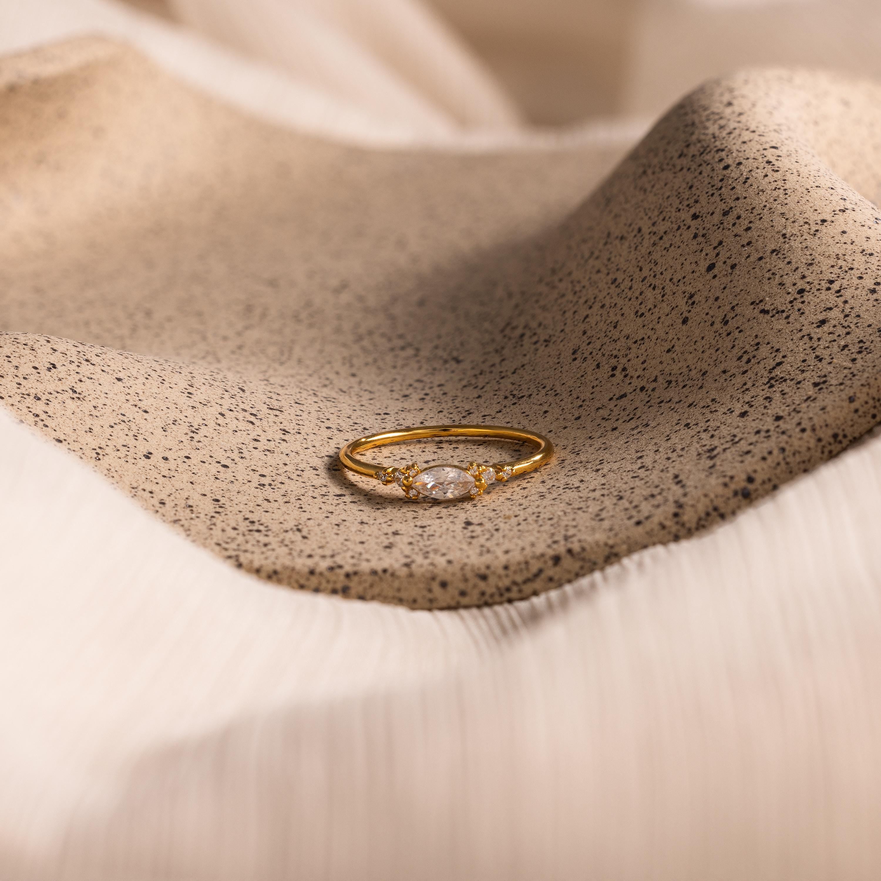 The Marquise Diamond Ring is displayed elegantly on a textured beige fabric surface.
