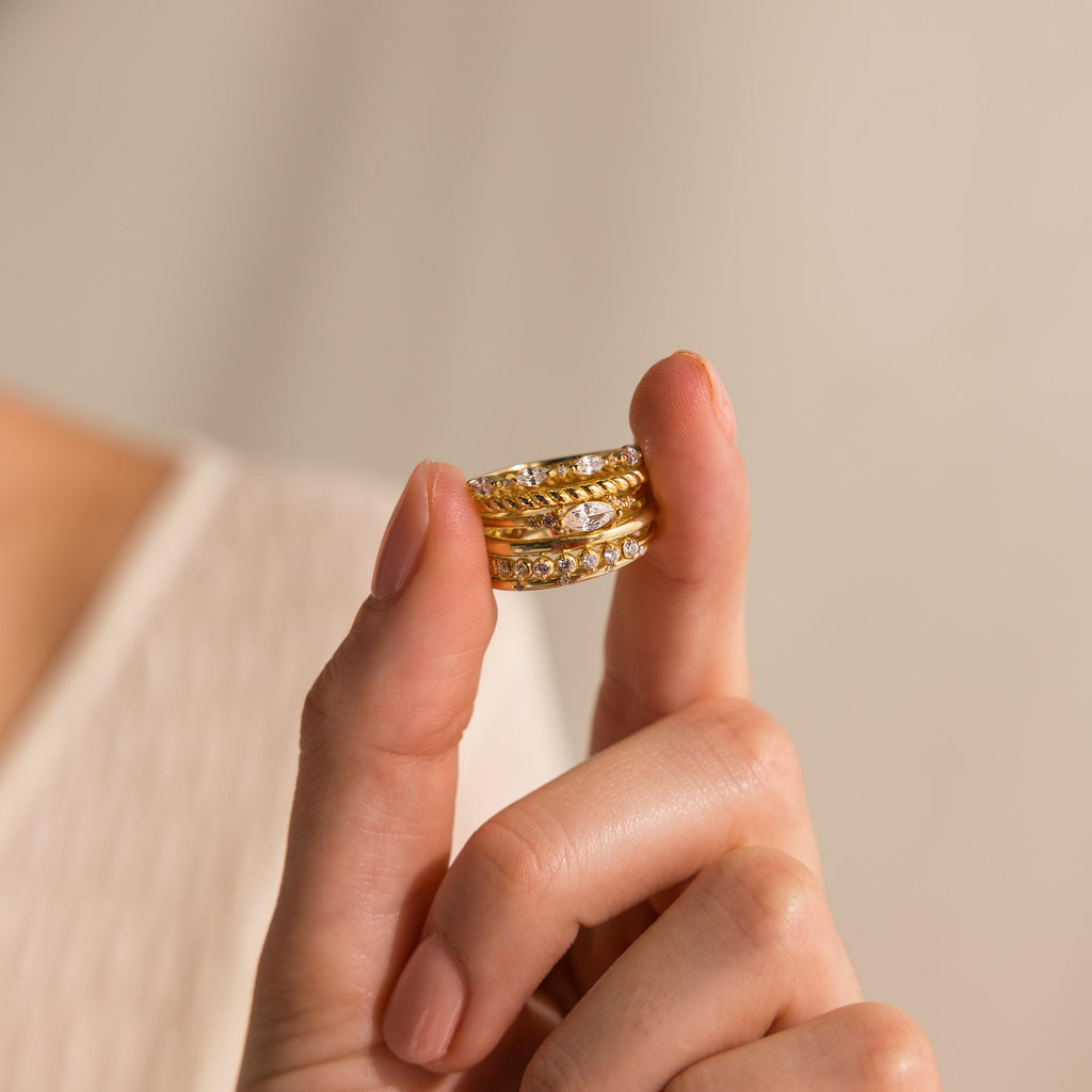 A hand displays three stacked gold rings—including the Marquise Diamond Ring with sparkling accents—against a neutral background.