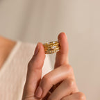 A hand displays three stacked gold rings—including the Marquise Diamond Ring with sparkling accents—against a neutral background.