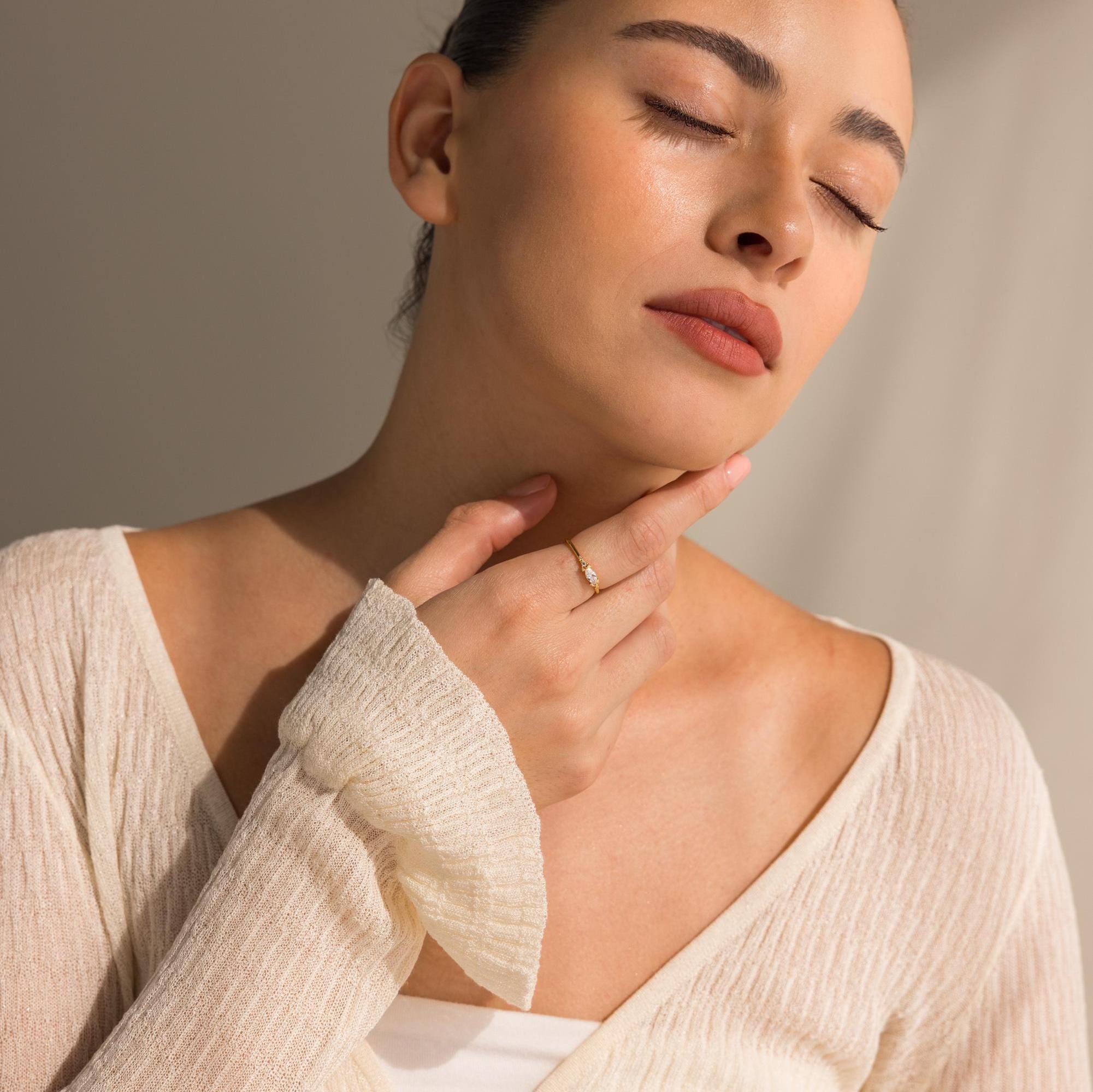 A woman in a cream sweater with eyes closed gently touches her neck, showcasing the Marquise Diamond Ring.