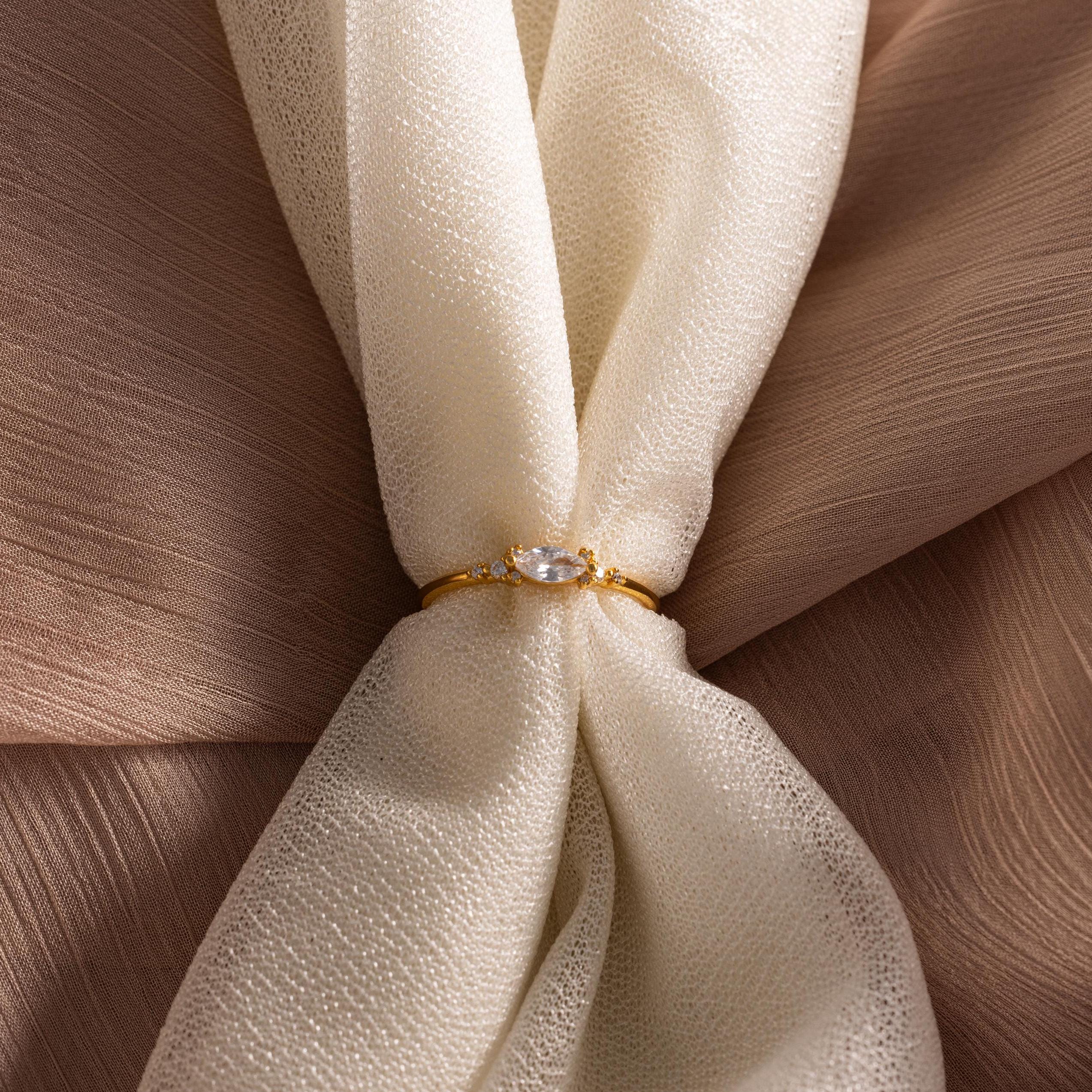 The Marquise Diamond Ring, featuring a gold finish band, is displayed on textured cream-colored fabric.