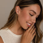Smiling woman in a sleeveless top showcases Butterfly Drop Huggies, elegant gold butterfly earrings, along with a gold ring adorned with small stones.
