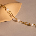 The Pearl Station Paperclip Bracelet, displayed on a smooth beige stone against a neutral background, is an elegant choice for those seeking refined birthstone jewelry.
