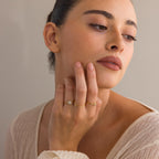 A woman with dark hair touches her face, wearing the Classic Pave Ring Set and a cream textured top, gazing to the side.