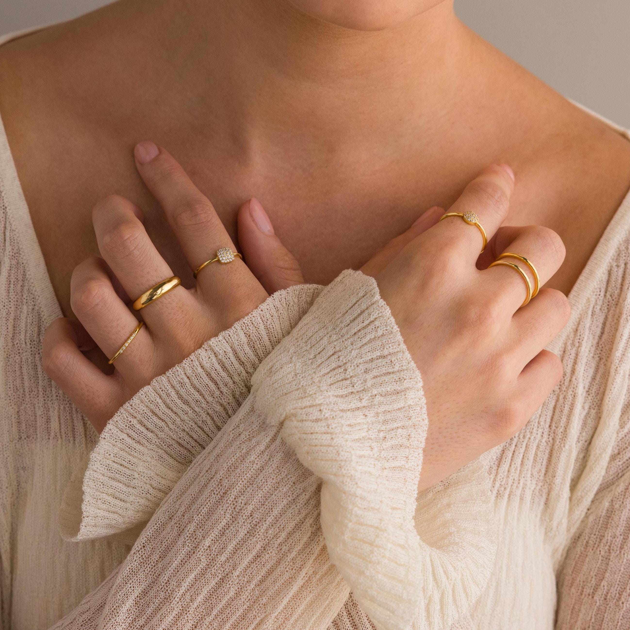A woman wearing a cream sweater showcases elegant gold jewelry, including the Classic Pave Ring Set, with her hands crossed on her chest.