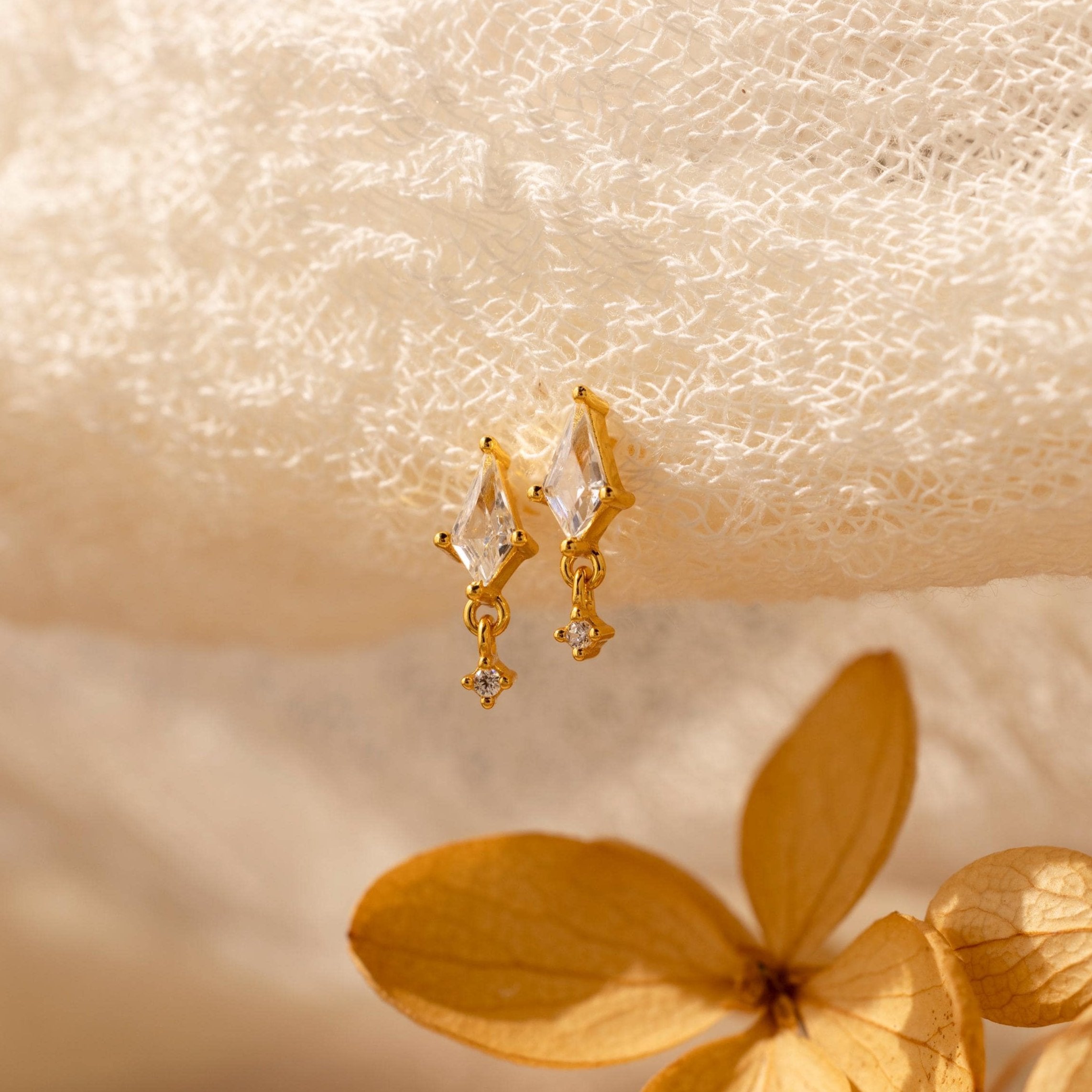 Diamond Kite Drop Earrings displayed on textured white fabric with a dried flower nearby, exuding vintage charm.