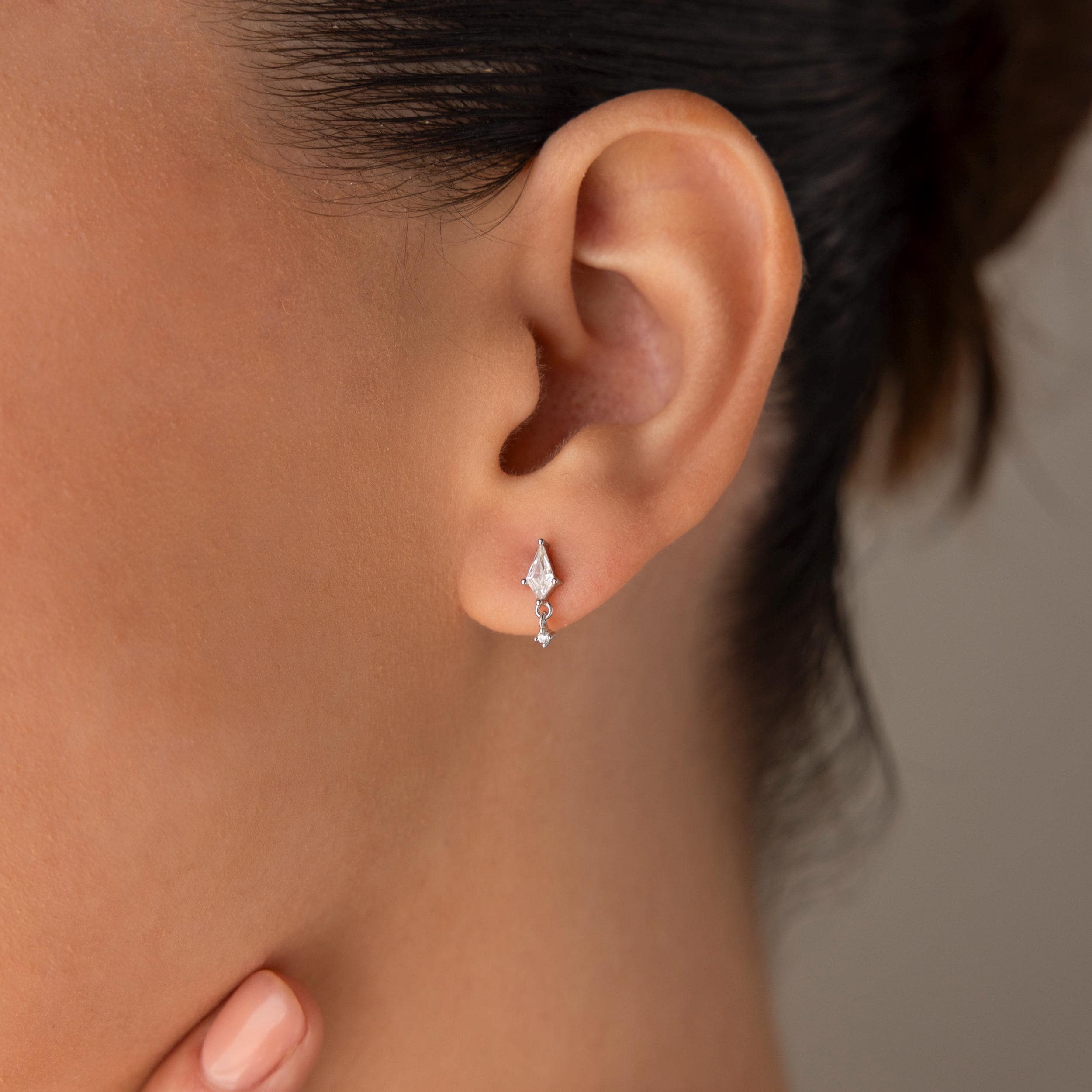 Close-up of a woman's ear wearing Diamond Kite Drop Earrings—delicate silver studs with small dangling gems that add subtle vintage charm to her look.