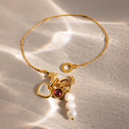 Hinged Circle Charm Bracelet in 18K Gold with heart, red gem, pearl charms, and antler design displayed on a sunlit, textured surface—ideal for minimalist jewelry lovers.