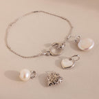The Hinged Circle Charm Bracelet in Sterling Silver, adorned with pearl and heart charms and paired with two extra pearl and heart pendants, is beautifully displayed on a beige surface.