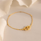 The Hinged Circle Charm Bracelet in 18K Gold features two interlocking loops and rests on a soft, light-colored surface—an ideal accessory for minimalist jewelry lovers.