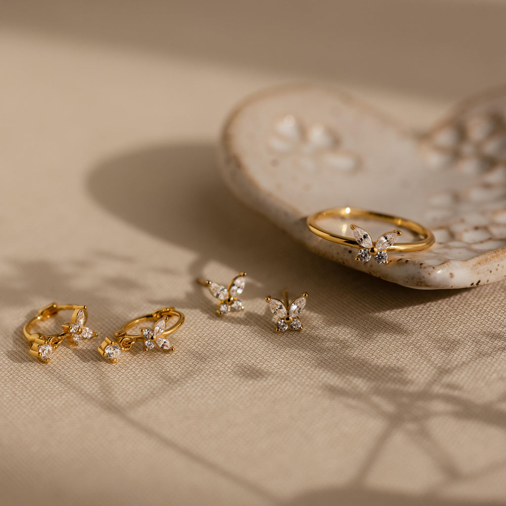 Butterfly Drop Huggies displayed on a beige surface with a ceramic dish in the background, featuring elegant butterfly-inspired earrings accented with sparkling diamonds.