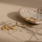 Butterfly Drop Huggies displayed on a beige surface with a ceramic dish in the background, featuring elegant butterfly-inspired earrings accented with sparkling diamonds.