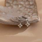 The Pearl Ivy Flower Huggies in Sterling Silver feature two silver hoop earrings with pearl drops and crystal accents, displayed on a textured ceramic dish to add a delicate floral touch to your jewelry collection.