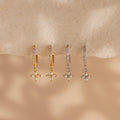 Two pairs of Pearl Ivy Flower Huggies—one gold, one silver—feature small pearl cluster charms resembling delicate florals, displayed on a beige surface.