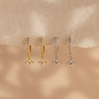 Two pairs of Pearl Ivy Flower Huggies—one gold, one silver—feature small pearl cluster charms resembling delicate florals, displayed on a beige surface.