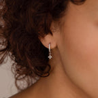 Close-up of a woman with curly hair wearing Pearl Ivy Flower Huggies in Sterling Silver—elegant drop earrings featuring a delicate floral design.