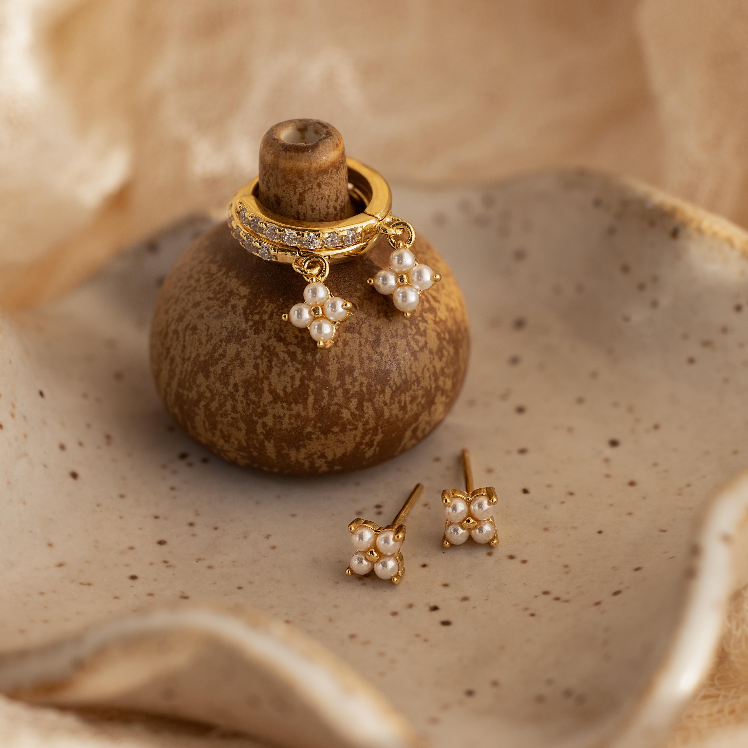 The Pearl Ivy Flower Studs in 18K Gold are displayed on a rustic brown holder with a beige ceramic dish background—an elegant choice for wedding jewelry.