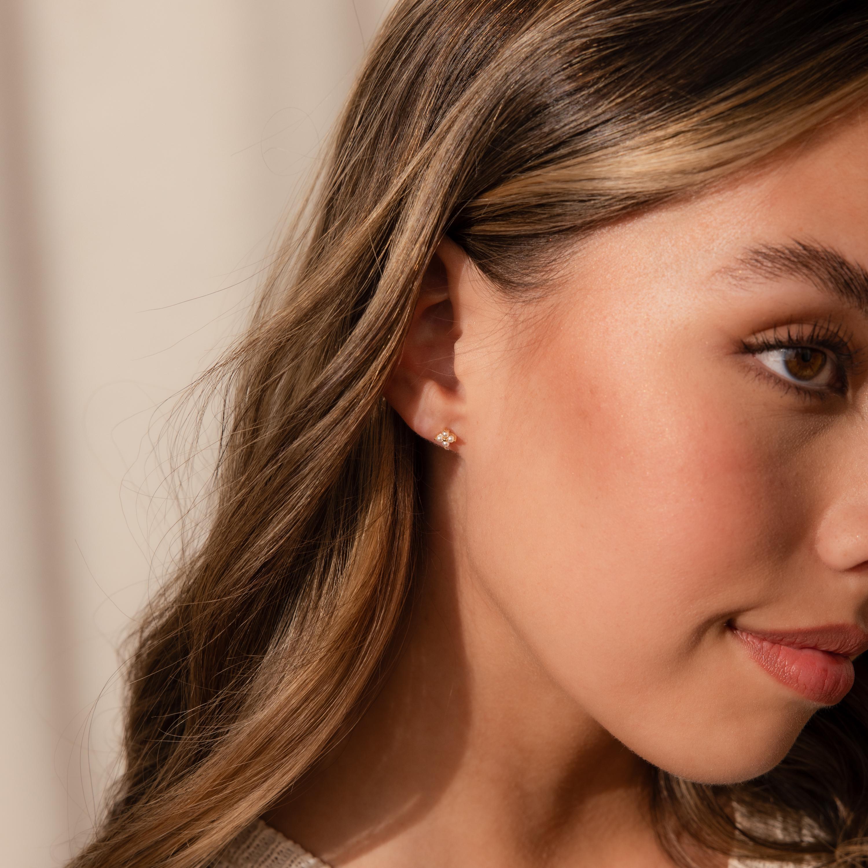 Close-up of a woman with long brown hair wearing delicate Pearl Ivy Flower Studs, elegant gold earrings shaped like flowers.
