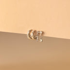 The Dainty Pave Earrings Set, featuring three gold hoop earrings and a dangling diamond-accented earring, is beautifully displayed on a beige background.