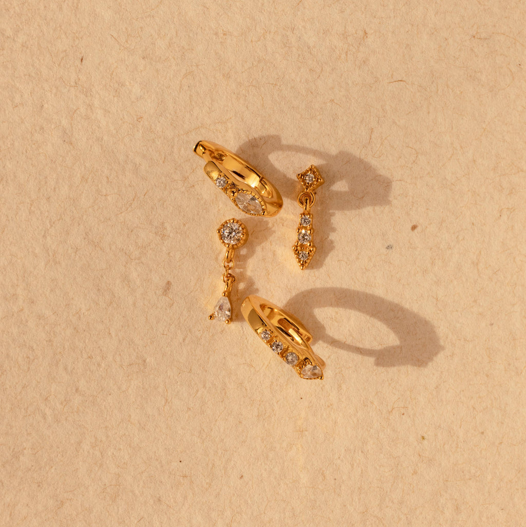 The Dainty Pave Earrings Set features sparkling pave accents and a chic design, displayed on a textured beige background—ideal for fans of elegant earrings.