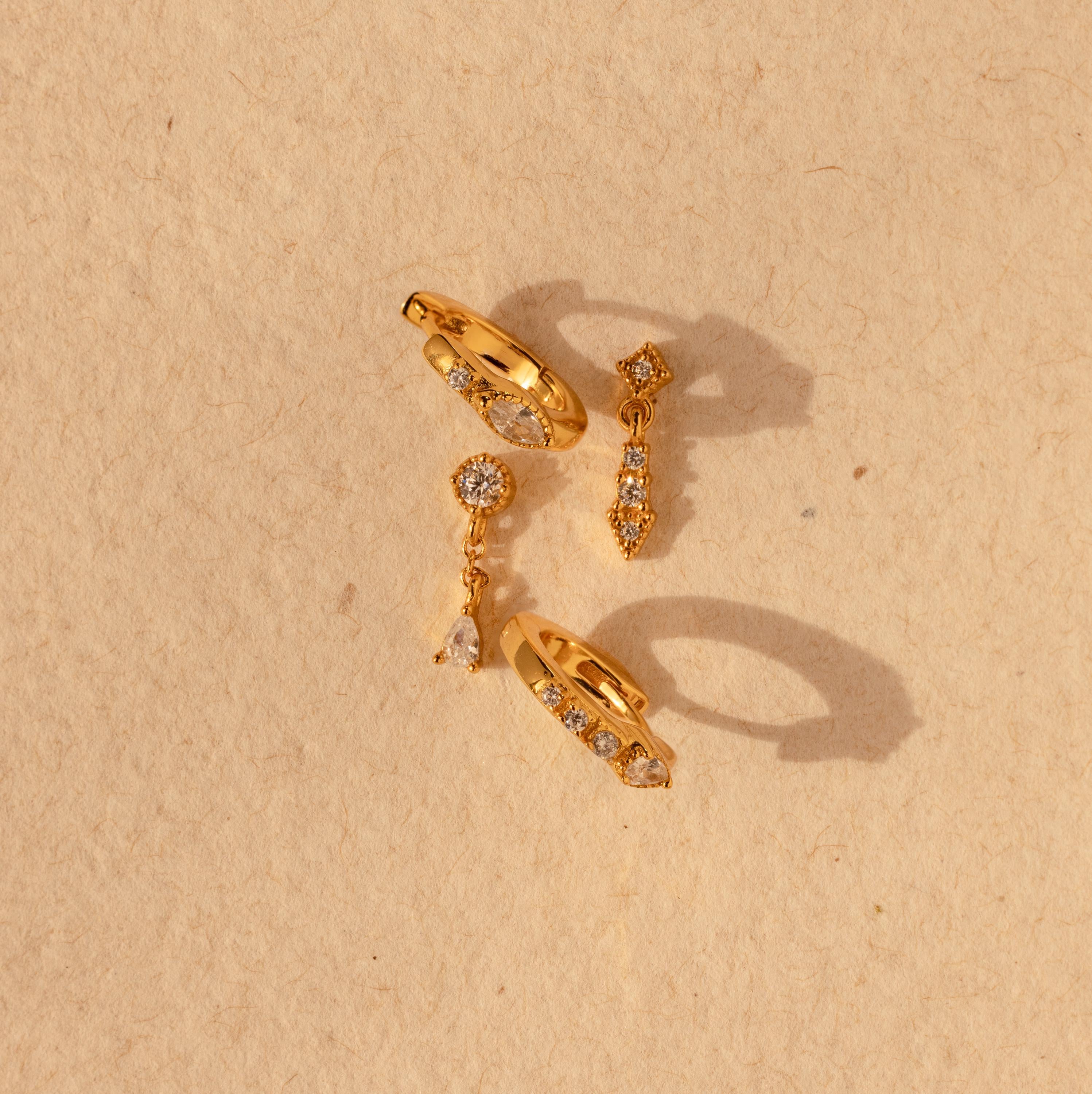 The Dainty Pave Earrings Set features sparkling pave accents and a chic design, displayed on a textured beige background—ideal for fans of elegant earrings.