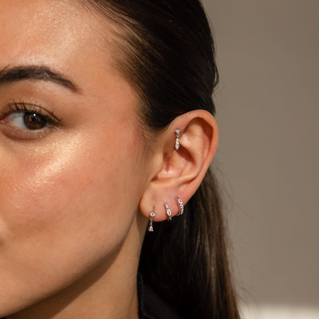 Close-up of a woman's ear adorned with the Dainty Pave Earrings Set, featuring multiple silver and diamond earrings in sparkling stud and pave designs.
