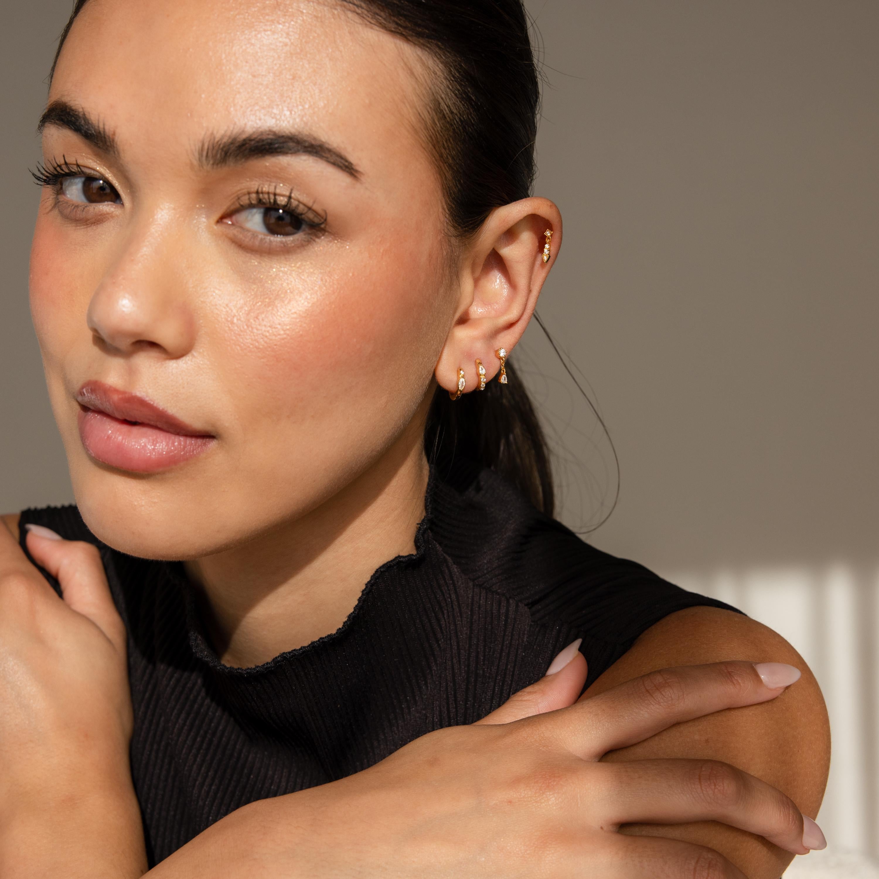A woman with glowing skin wears the Dainty Pave Earrings Set and a black sleeveless top, arms crossed over her chest.