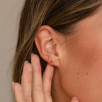 Close-up of a woman's ear wearing Ruby Flatback Studs, her hand gently touching her earlobe.