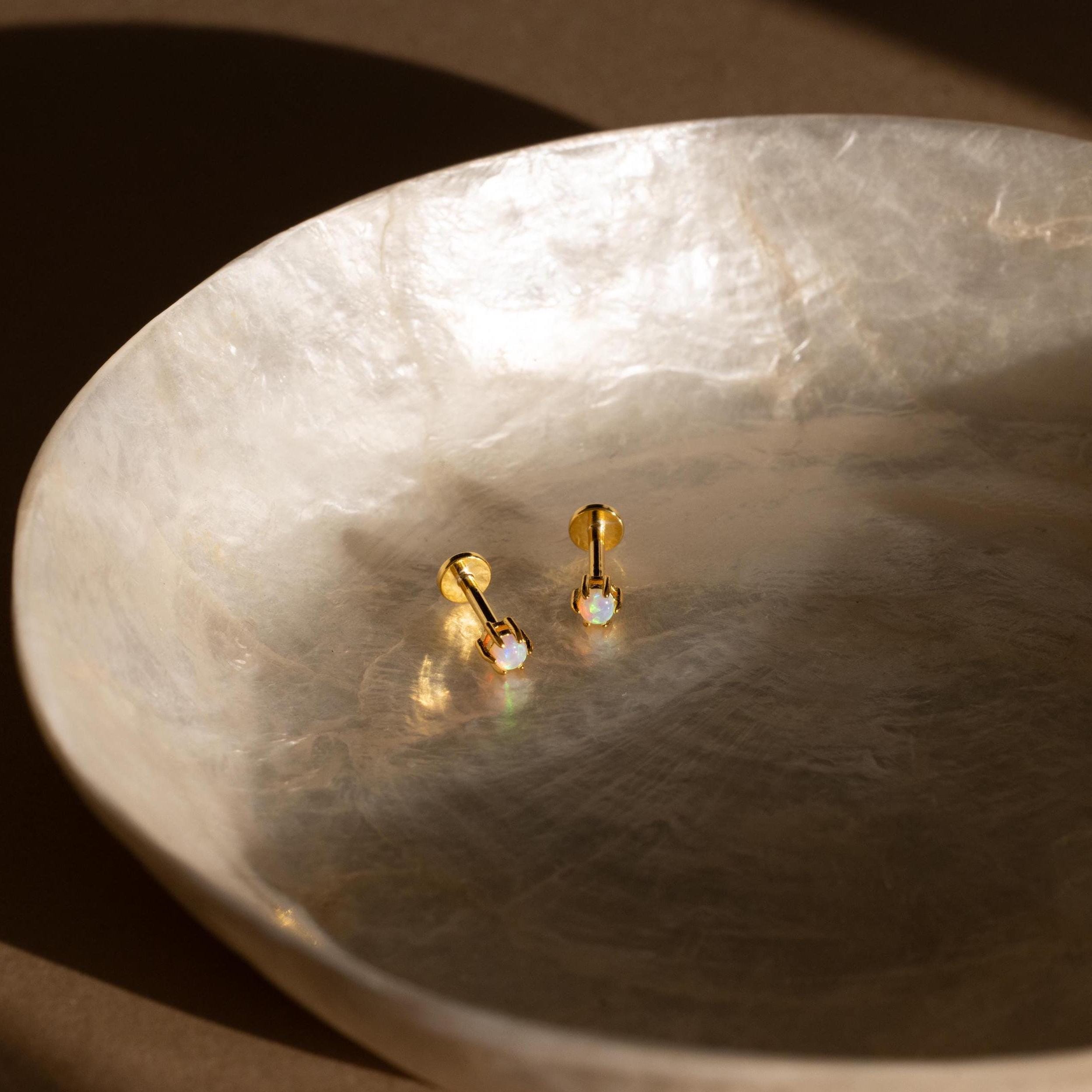 Opal Flatback Studs, featuring iridescent stones, are displayed in a textured, round, light-hued dish set on a brown surface.