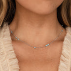 A woman wears the Turquoise Satellite Necklace featuring small turquoise beads, ideal for layering, paired with a cream textured top.