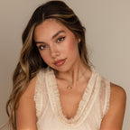Young woman with long wavy hair wears a sleeveless cream ruffled top and the Turquoise Satellite Necklace, featuring turquoise beads, posing calmly.
