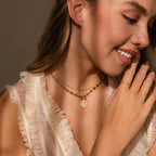 Smiling woman in a cream ruffled top wearing gold jewelry, featuring the Evil Eye Toggle Necklace.