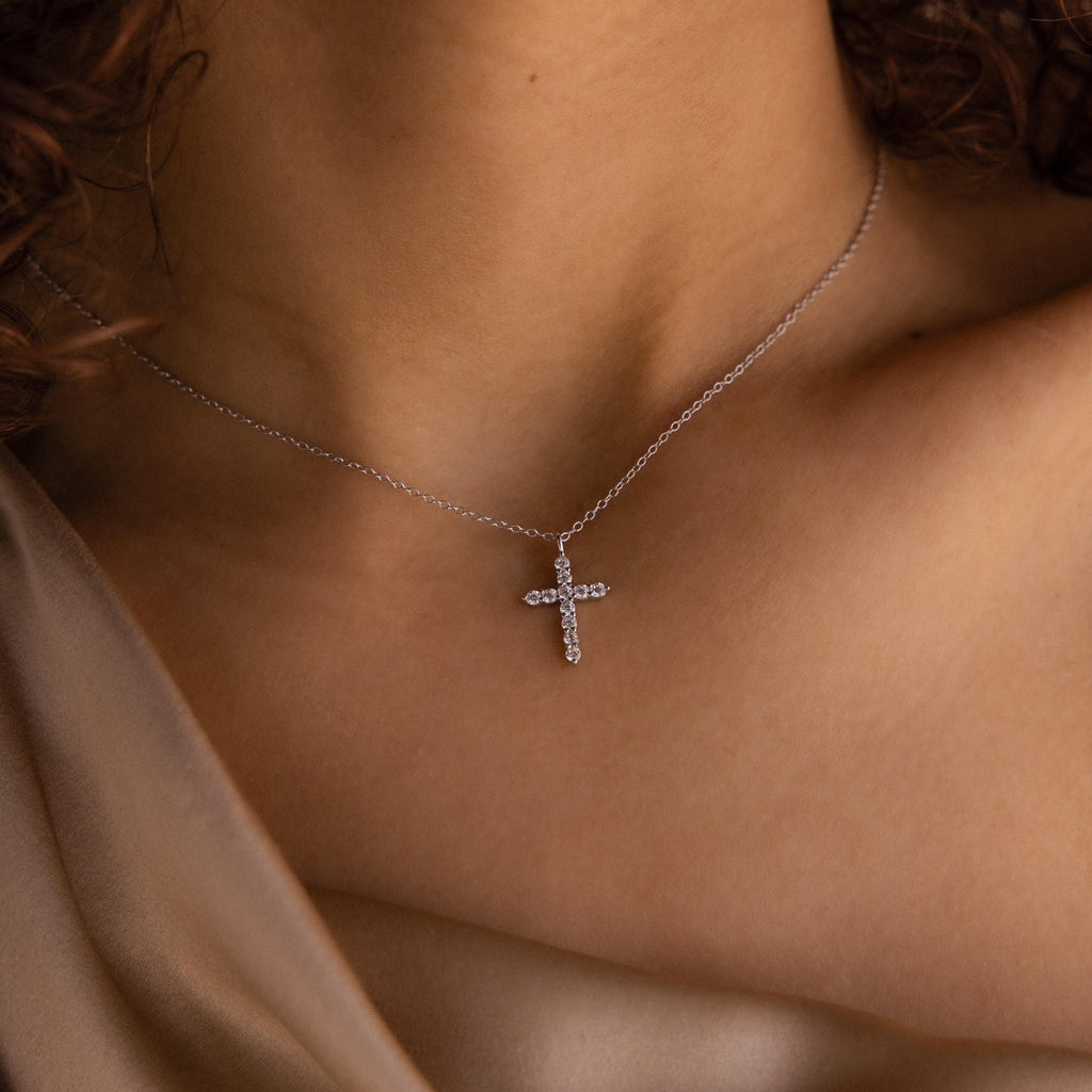 A woman wears the elegant Pave Cross Necklace against her bare upper chest, paired with a beige satin top.