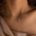 A woman wears the elegant Pave Cross Necklace against her bare upper chest, paired with a beige satin top.