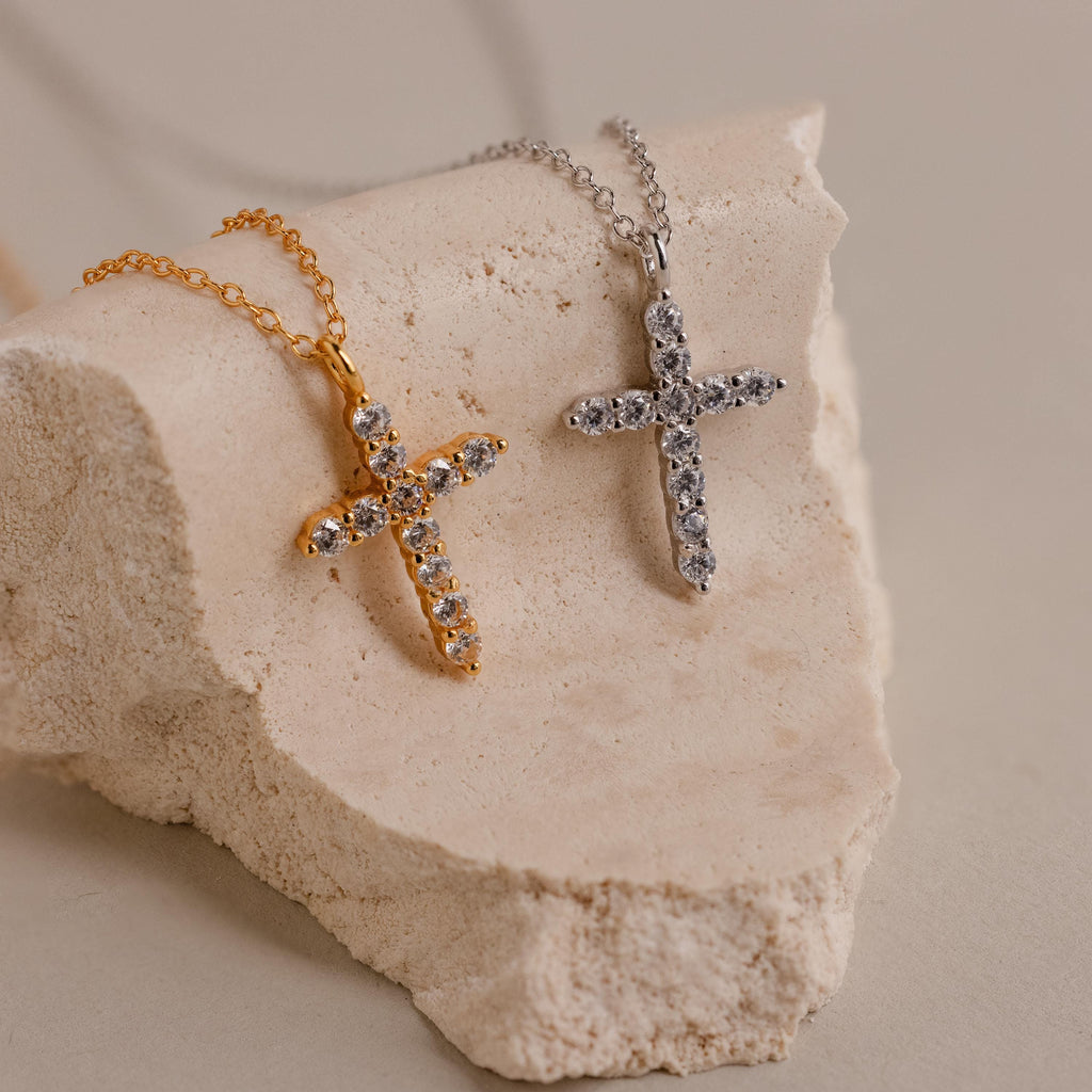 Gold and silver Pavé Cross Necklaces with sparkling stones, elegantly displayed on a textured stone block—a dazzling jewelry selection.
