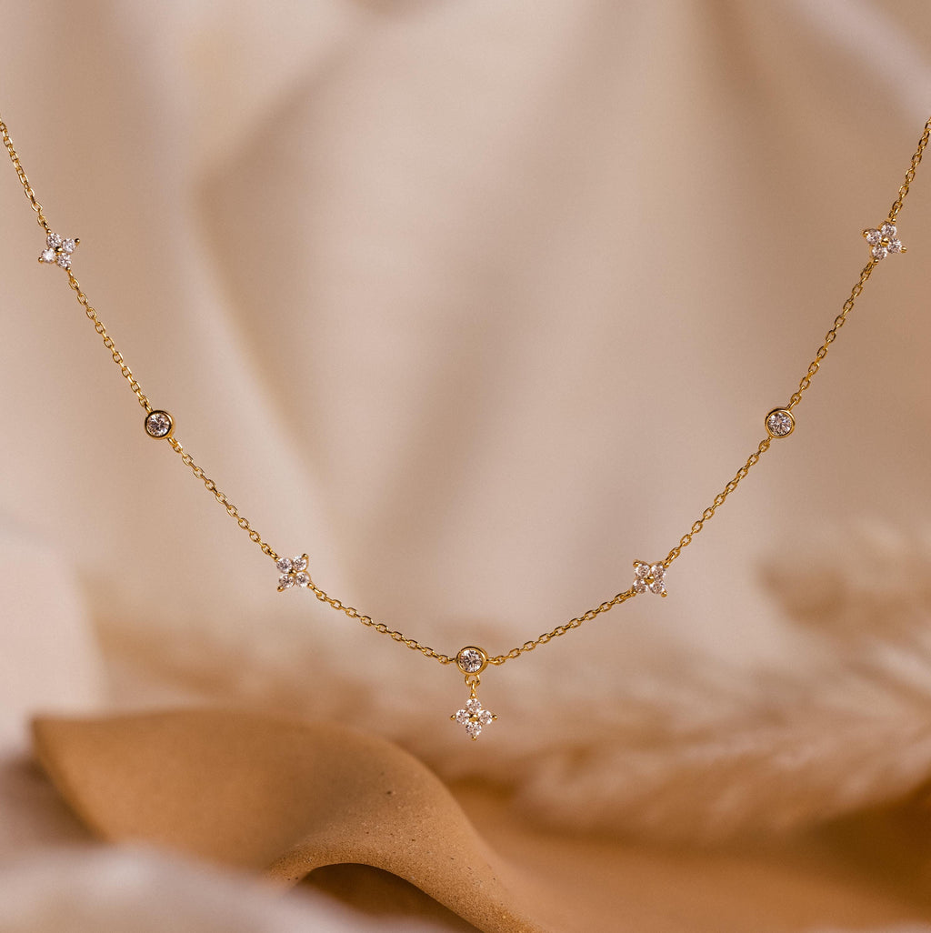 The Ivy Diamond Station Necklace features small star and diamond accents, elegantly displayed on a soft beige fabric background.