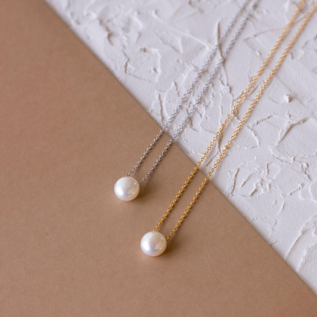 The Classic Pearl Pendant Necklace is displayed elegantly alongside dainty chain styles on a surface.