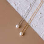 The Classic Pearl Pendant Necklace is displayed elegantly alongside dainty chain styles on a surface.