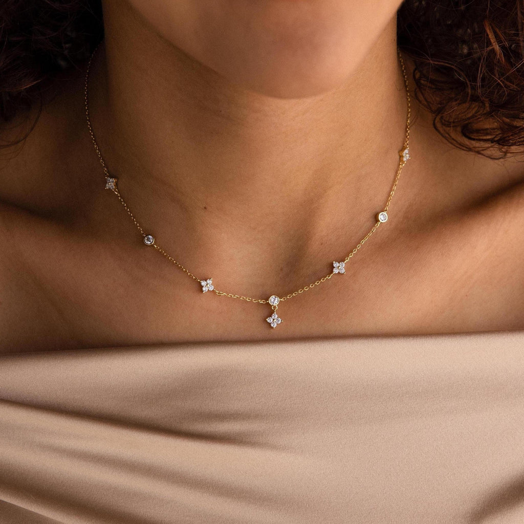 A woman wears the Ivy Diamond Station Necklace, a delicate gold necklace with sparkling diamond accents, styled with an off-shoulder beige top.