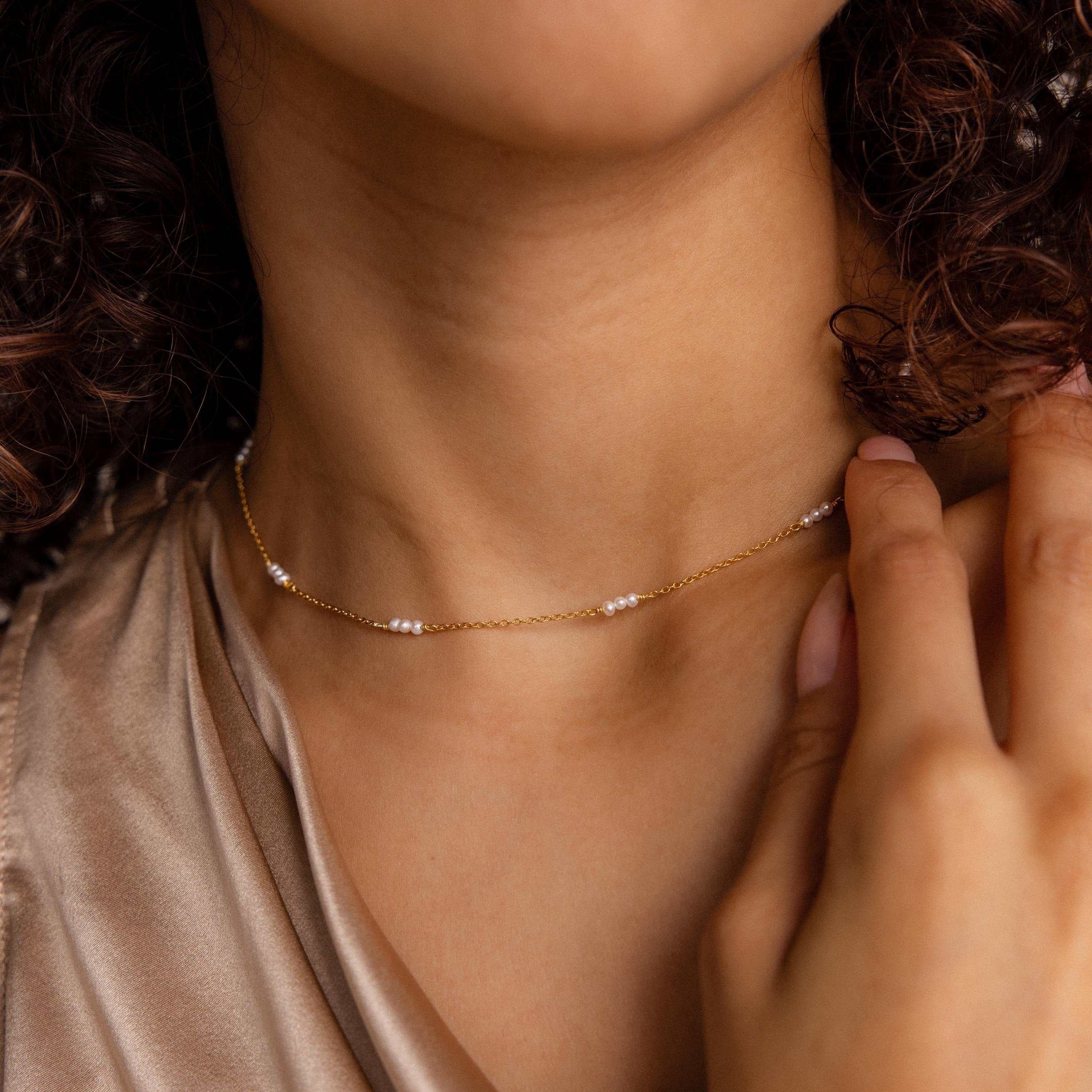 A woman gently touches the Hali Pearl Station Necklace near her neck, highlighting the elegance of minimalist jewelry.