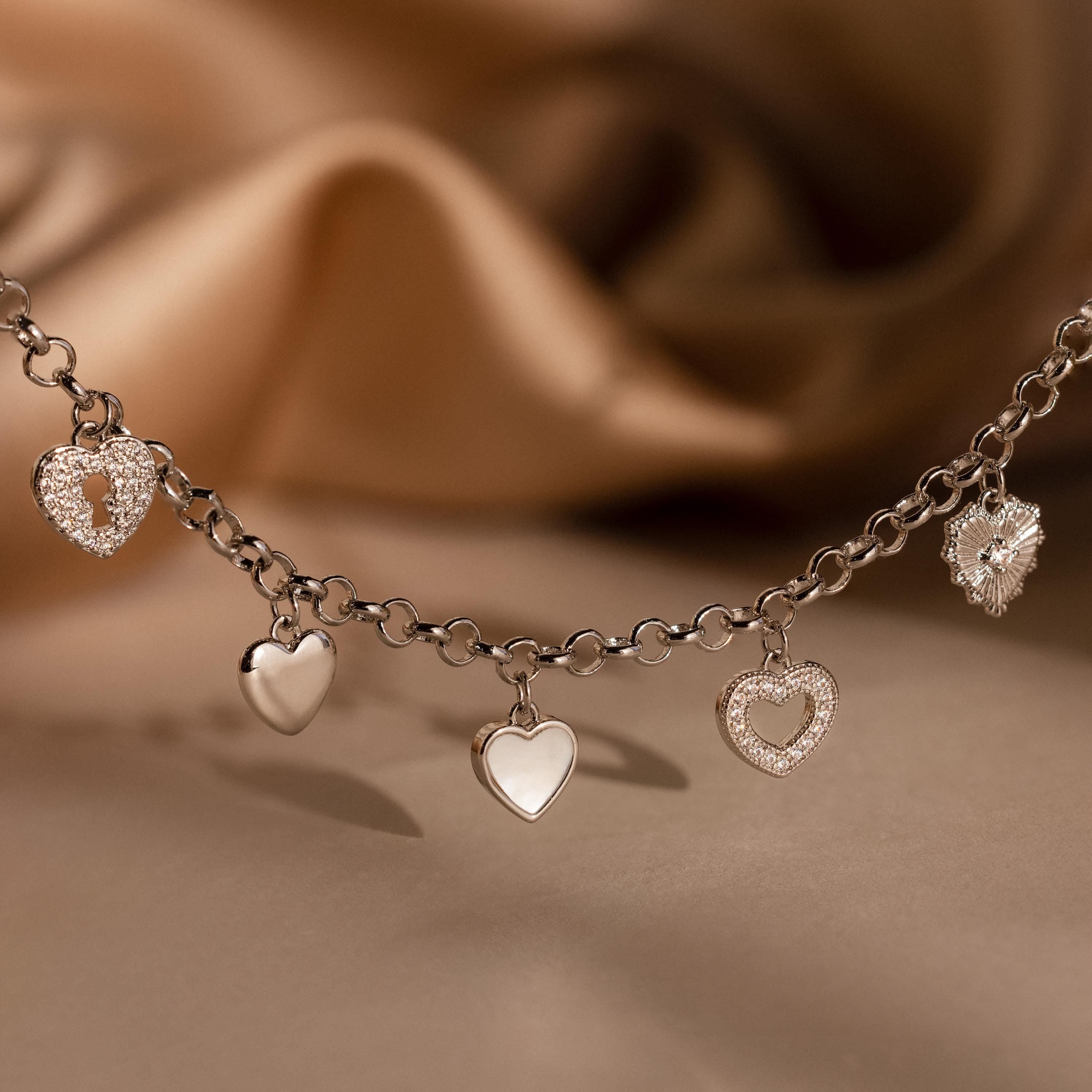 Heart Charm Bracelet in Sterling Silver with five heart charms displayed on a soft brown fabric background—a perfect gift for your girlfriend.