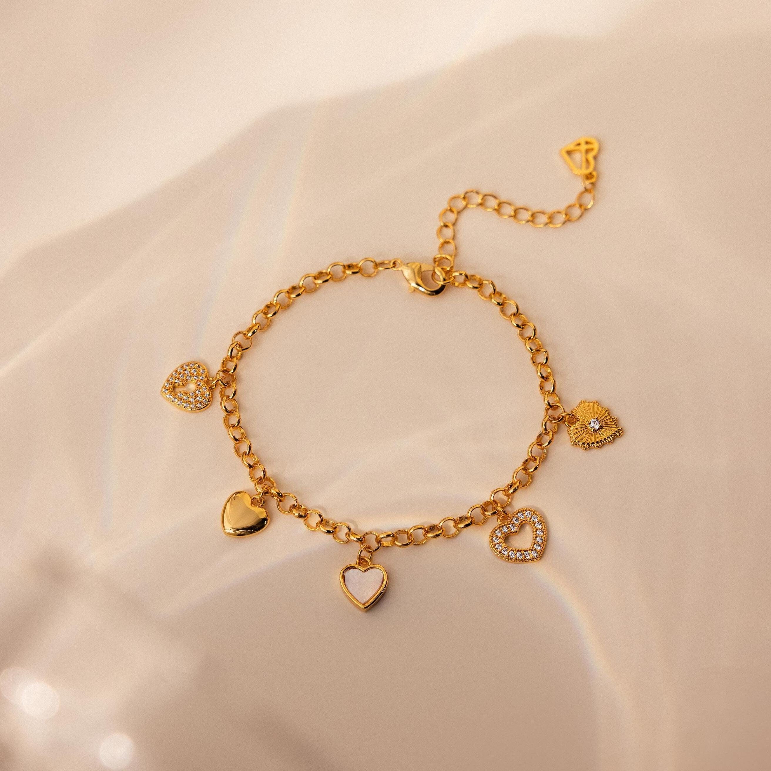 The Heart Charm Bracelet features delicate heart charms and is shown on a soft beige background—making it the perfect gift for your girlfriend.