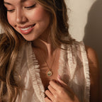Smiling woman with long hair wearing a ruffled white top and the Abalone Sunrise Pendant Necklace in 18K Gold, looking down.
