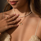 A woman gently touches her jewelry—a Classic Pearl Heart Charm necklace and matching ring.