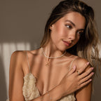 Woman with long hair in a cream dress poses in soft natural light, wearing the Classic Pearl Heart Charm in Sterling Silver and gold jewelry.