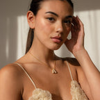 A woman touches her hair, sunlight on her face, wearing a beige floral top and the Pave Puff Letter Necklace in White Gold.