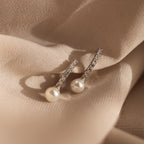 The Pave Pearl Drop Huggies, featuring sparkling diamonds and luminous pearls, are showcased elegantly on beige fabric.