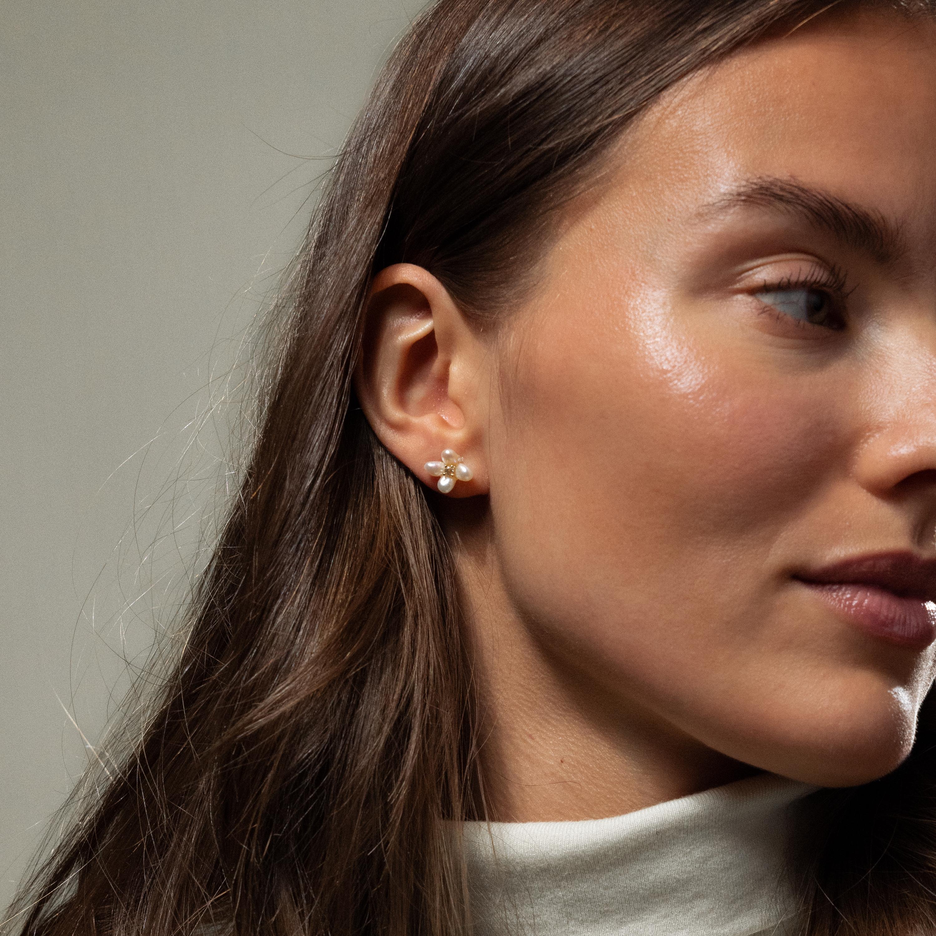 Woman with long brown hair, wearing Pearl Flower Studs and a white turtleneck, faces sideways.