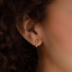 Close-up of a person’s ear wearing Diamond Starburst Drop Studs in 18K Gold, featuring two dangling star-shaped charms that shimmer like diamonds.